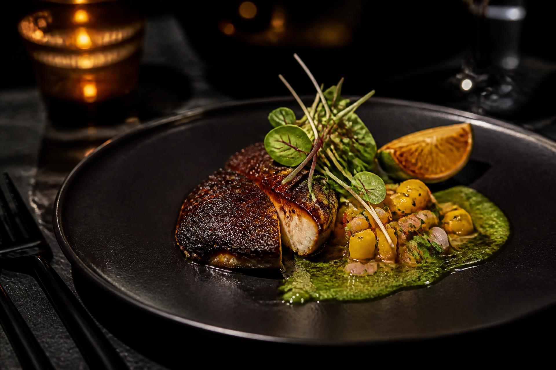 Fine-dining course plated on dark ceramic by candlelight